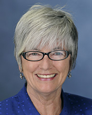A portrait of Professor Anne Hedeman. Hedeman has short, silvery hair and is wearing glasses and a blue blouse.