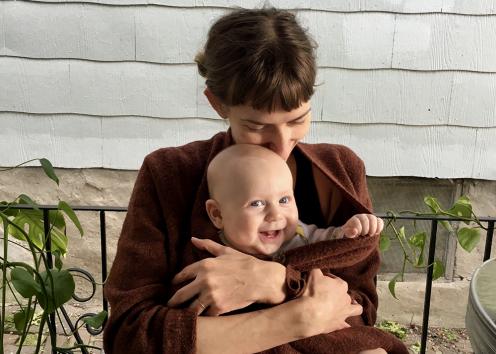 Rebekah sits in her wheelchair with a smiling, bald baby tucked in her massive brown sweater. She rests her lips and cheek against his fuzzy head.